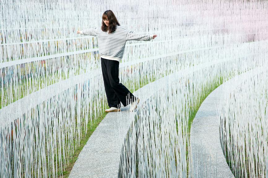 A woman on Friday walks through an installation by artist Yu Wen-fu consisting of 100,000 pink bamboo sticks representing tung blossoms that have fallen to the ground at the Taiwan Hakka Museum in Miaoli County’s Tongluo Township.